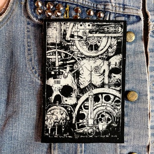 May include: Black and white embroidered patch featuring a skull, gears, and other mechanical imagery. The patch has the text "LEWIS MYHEM" at the bottom.
