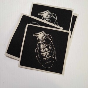 May include: A stack of four black fabric patches with a white image of a grenade on each patch.