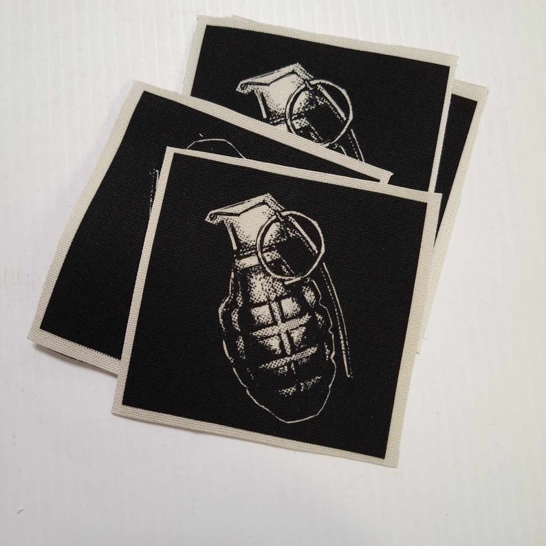 May include: A stack of four black fabric patches with a white image of a grenade on each patch.