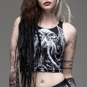 May include: Black crop top with a white graphic print of a creature with tentacles. The model is wearing the top with black pants and has black and white dreadlocks.