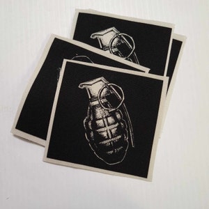 May include: Three black fabric patches with a white image of a hand grenade on each. The patches are stacked on top of each other.