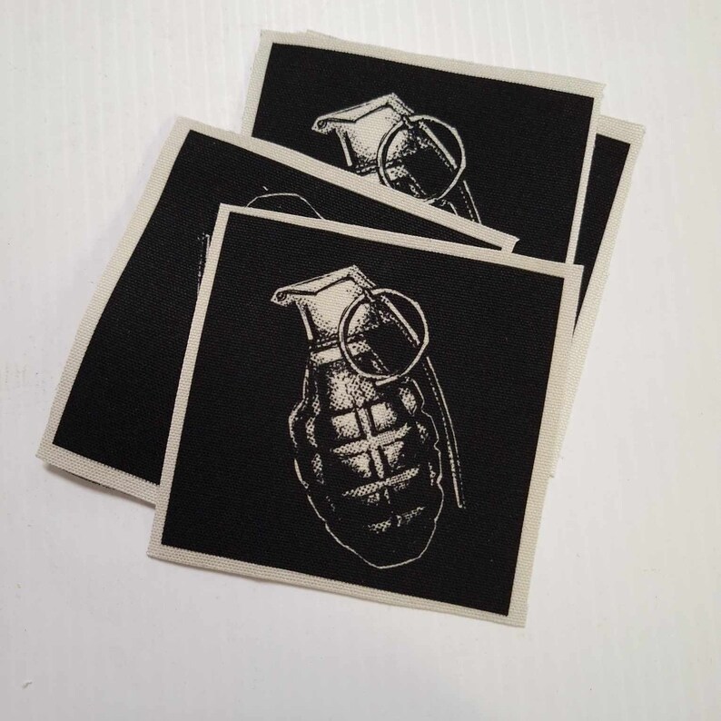 May include: Three black fabric patches with a white image of a hand grenade on each. The patches are stacked on top of each other.