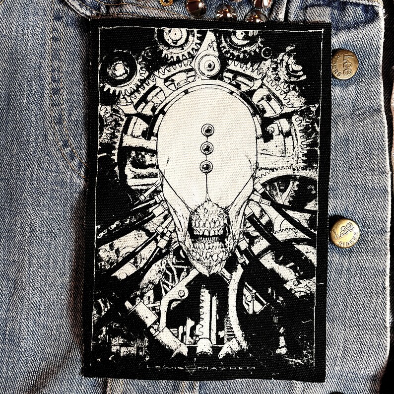 May include: Black and white patch featuring a detailed illustration of a skull with gears and machinery. The text "LEWIS MAYHEM" is at the bottom of the patch.