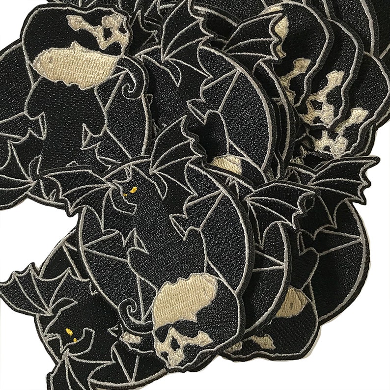 Pode incluir: Um monte de patches de ferro bordados em preto e branco com uma caveira com asas de morcego. A caveira &eacute; delineada em branco e tem um olho branco. As asas de morcego tamb&eacute;m s&atilde;o delineadas em branco.