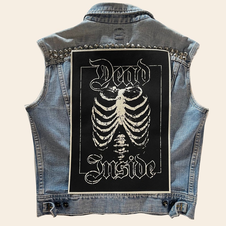 May include: A blue denim vest with silver studs and a black patch on the back. The patch features a white skeleton with the words "Dead Inside" in a gothic font.
