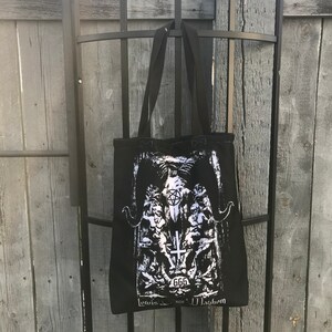 May include: Black canvas tote bag with a white graphic print of a pentagram, skull, and the text "666 Lotus Mayhem".