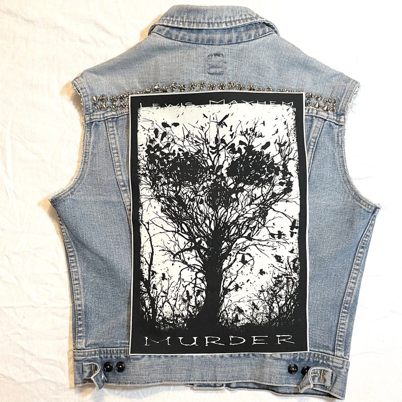 K&ouml;nnte beinhalten: Eine hellblaue Jeansweste mit einem schwarzen und wei&szlig;en Patch auf der R&uuml;ckseite. Der Patch zeigt einen Baum mit V&ouml;geln und den Text "Lewis Mayhem Murder".