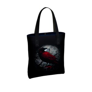 May include: Black tote bag with a red crow perched on a branch in front of a full moon. The crow has black wings and a red body.