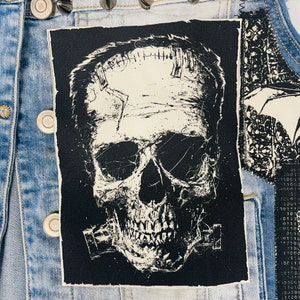 Op de afbeelding: Zwart-witte strijkpatch met een schedel met hechtingen op het voorhoofd. De schedel is in een distressed stijl met een witte omtrek.