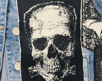 Puede incluir: Parche termoadhesivo en blanco y negro con una calavera con puntadas en la frente. La calavera está en un estilo desgastado con un contorno blanco.