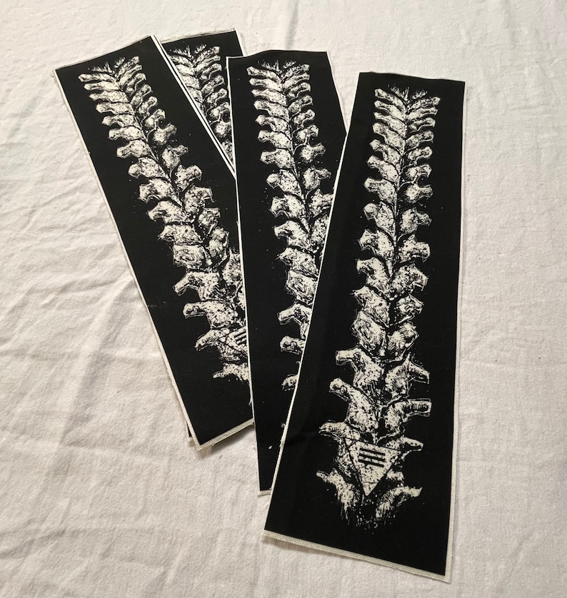Op de afbeelding: Vier zwart-witte anatomische illustraties van de wervelkolom, gedrukt op stof. De wervelkolom is gedetailleerd en realistisch afgebeeld.