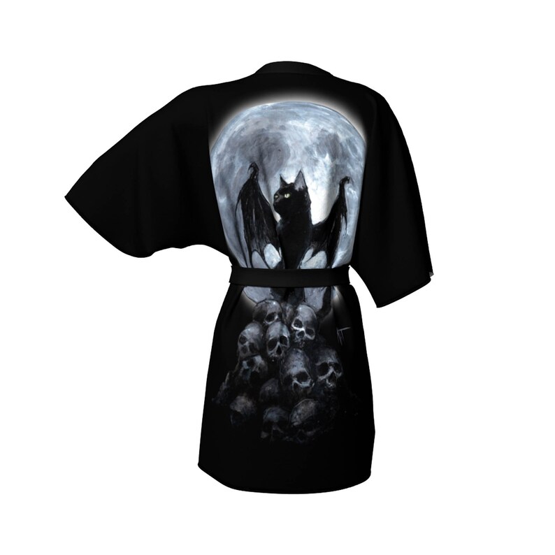 May include: Black and white robe with a graphic print of a black cat with bat wings standing on a pile of skulls in front of a full moon.