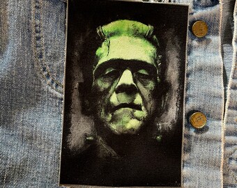 Puede incluir: Un parche bordado negro y verde con un primer plano de la cara de Frankenstein.