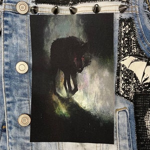 K&ouml;nnte beinhalten: Schwarzer und wei&szlig;er Wolf-Patch mit roten Augen vor einem dunklen, nebligen Hintergrund. Der Wolf steht auf einem grasbewachsenen H&uuml;gel.