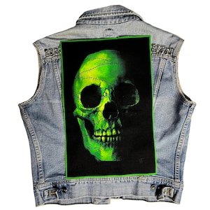 Peut inclure: Un crâne vert avec des points de suture sur un fond noir. Le crâne est sur un gilet en jean avec des clous argentés.