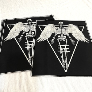 K&ouml;nnte beinhalten: Zwei schwarze Stoffpatches mit einem wei&szlig;en Skelett mit Fl&uuml;geln in einem wei&szlig;en Dreieck. Das Skelett tr&auml;gt eine Gasmaske und hat ein wei&szlig;es Kreuz dahinter.