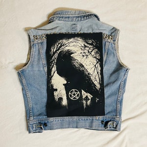 Op de afbeelding: Een denim vest met een zwarte patch waarop een kraai op een grafsteen met een pentagram zit. De patch is op de achterkant van het vest genaaid.