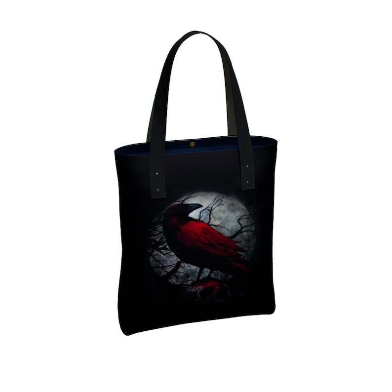 May include: Black tote bag with a red crow perched on a branch in front of a full moon. The crow is silhouetted against the moon.