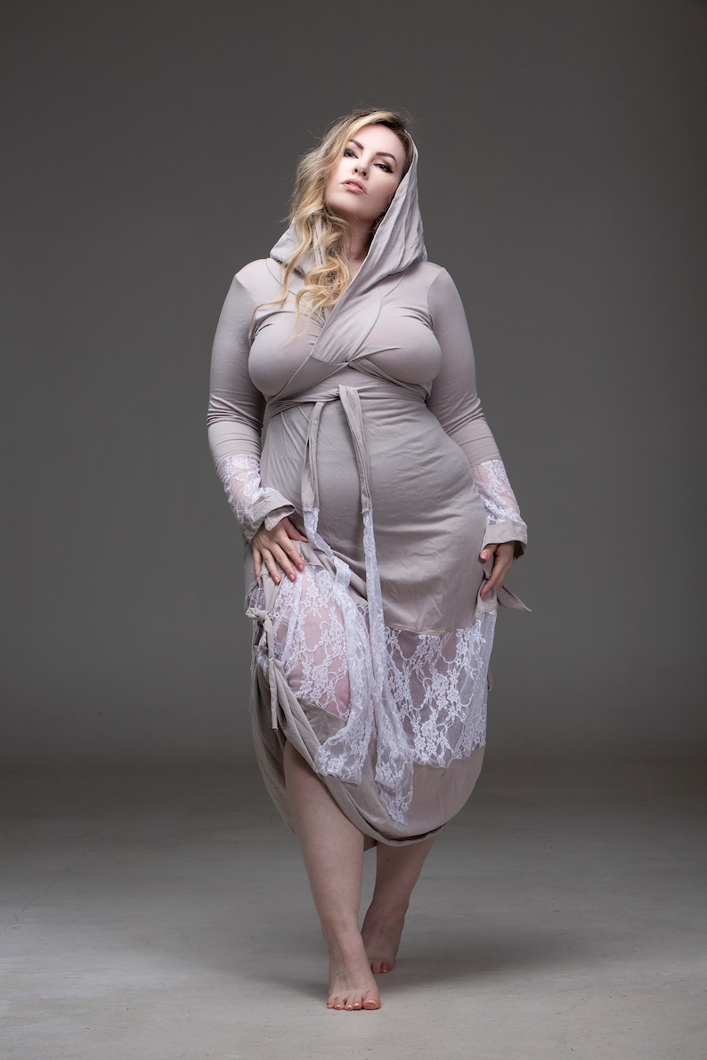 May include: A woman wearing a long, light gray hooded robe with a white lace trim. The robe is tied at the waist with a matching sash.