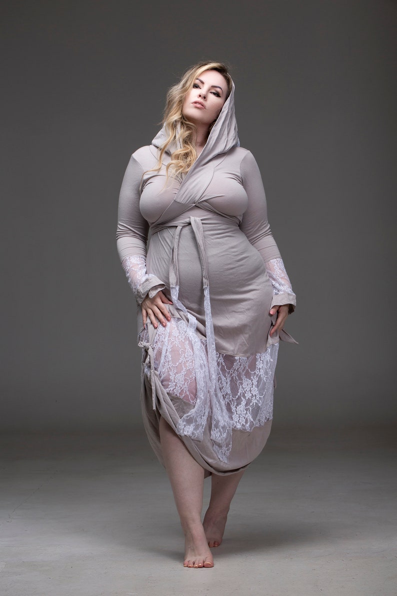 May include: A woman wearing a long, light gray hooded robe with a white lace trim. The robe is tied at the waist with a matching sash.
