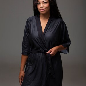 May include: A black satin robe with a shawl collar and a tie belt. The robe is worn by a person with long dark hair.