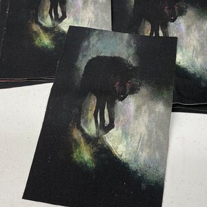 K&ouml;nnte beinhalten: Ein schwarzer Wolf mit leuchtend roten Augen geht durch einen nebligen Wald. Der Wolf ist auf einem schwarzen Stoffpatch gemalt.