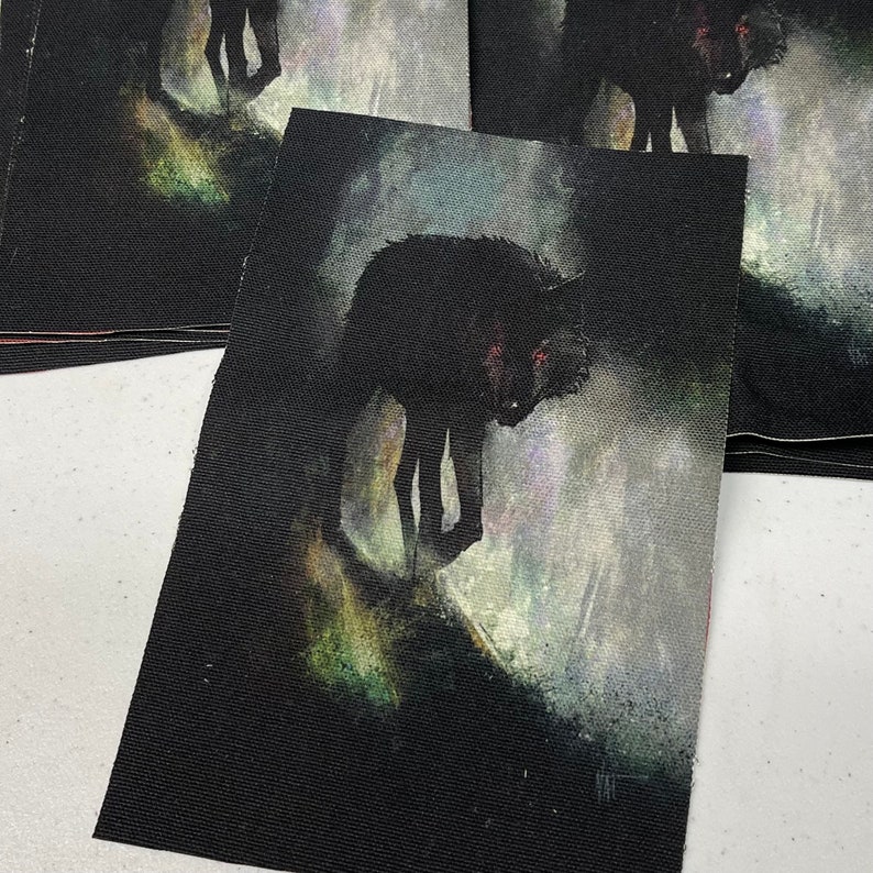 K&ouml;nnte beinhalten: Ein schwarzer Wolf mit leuchtend roten Augen geht durch einen nebligen Wald. Der Wolf ist auf einem schwarzen Stoffpatch gemalt.