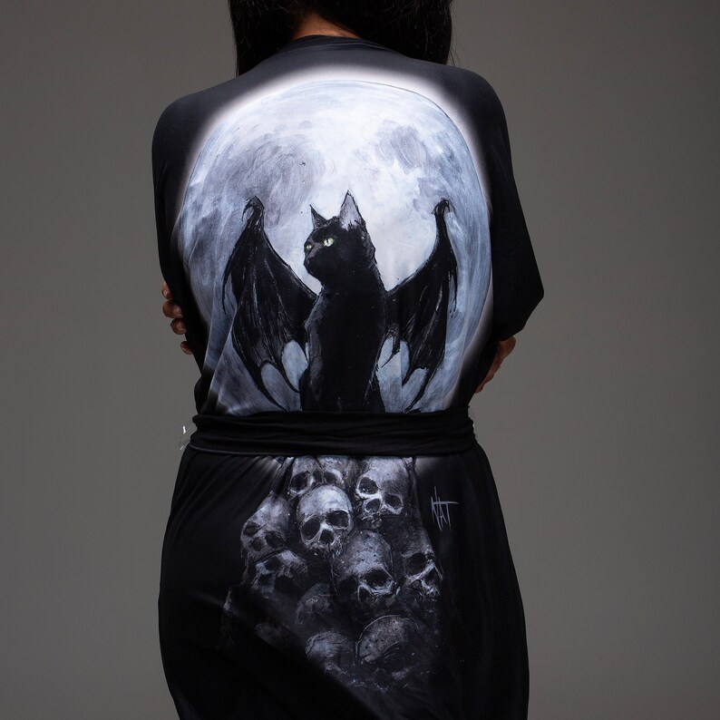May include: Black and white robe with a full moon and a black cat with wings on the back. The bottom of the robe has a skull pattern.