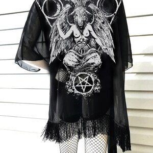 May include: Black sheer kimono with a white print of a goat-headed figure with wings and a pentagram. The kimono has black fringe around the bottom.