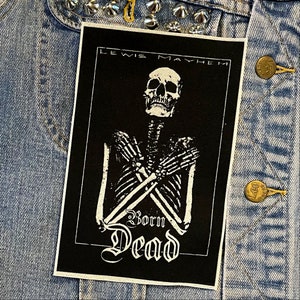 May include: Black and white iron-on patch featuring a skeleton with crossed arms and the text "Lewis Mayhem Born Dead".