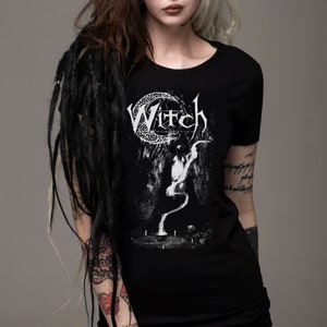 May include: Black t-shirt with a white graphic print of a witch with the word "Witch" above her. The graphic is surrounded by a crescent moon and a circle of decorative elements.