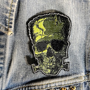 May include: Green and black embroidered iron-on patch of a Frankenstein skull with stitches on the forehead.