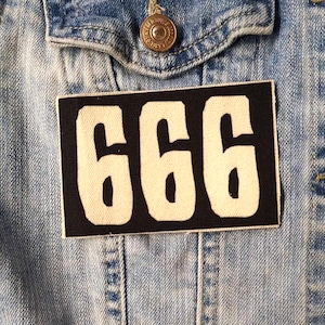 May include: A black and white patch with the number 666 in large white font. The patch is sewn onto a blue denim jacket.
