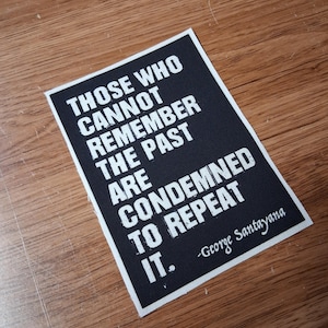 May include: A rectangular black patch with white text that reads: "THOSE WHO CANNOT REMEMBER THE PAST ARE CONDEMNED TO REPEAT IT." The quote is attributed to George Santayana.