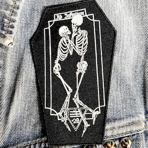 May include: Black and white embroidered patch featuring two skeletons embracing, with the text "Ad Infinitum" above them and a triangle with the number "29" below them.