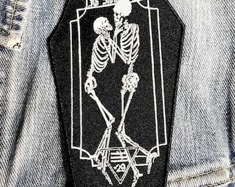 May include: Black and white embroidered patch featuring two skeletons embracing, with the text "Ad Infinitum" above them and a triangle with the number "29" below them.