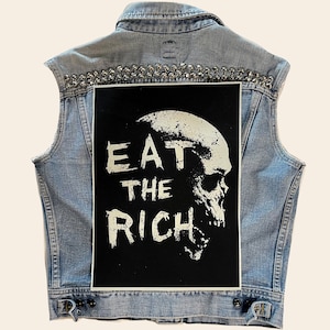 May include: A light blue denim vest with silver studs around the collar and a black patch on the back that says "EAT THE RICH" in white with a skull graphic.