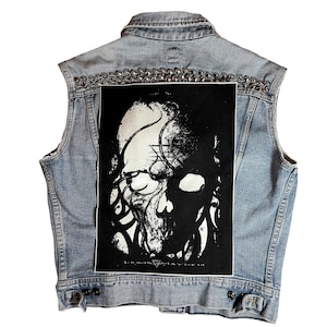 May include: A light blue denim vest with silver studs and a black patch featuring a white skull with tentacles and the text "Lewis Mayhem".