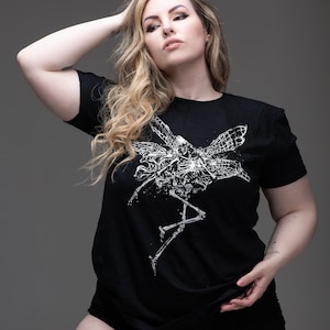 Könnte beinhalten: Schwarzes Kurzarm-T-Shirt mit weißer Skelett-Fee-Grafik. Das Design zeigt ein detailliertes Skelett mit insektenartigen Flügeln. Das Shirt besteht aus einem weichen Material und eignet sich für Freizeitkleidung.