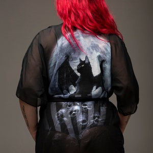 May include: Black sheer robe with a bat and moon print. The robe has a striped pattern underneath.