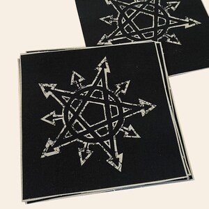 Puede incluir: Dos parches de tela negra con un dise&ntilde;o de estrella blanca. La estrella tiene una forma de pent&aacute;gono central con ocho puntos que irradian hacia afuera. Cada punto tiene un borde irregular y una forma de punta de flecha.