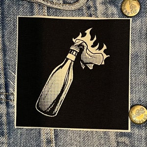May include: Black and white illustration of a Molotov cocktail on a black patch. The patch is made of fabric and has a white border.