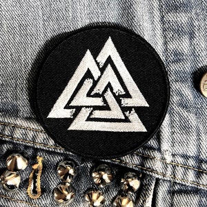 May include: Black and white embroidered patch featuring a triple triangle design. The patch is circular and has a black background.