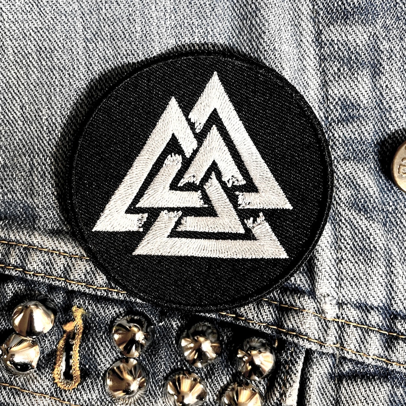 May include: Black and white embroidered patch featuring a triple triangle design. The patch is circular and has a black background.