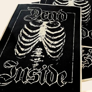 May include: Black and white patch with the text "Dead Inside" in a gothic font. A white ribcage graphic is centered on the patch.