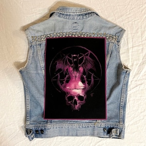 May include: A black denim vest with silver studs and a pink and black patch featuring a winged demon figure with a skull.