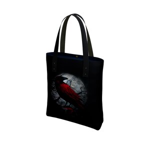 May include: Black tote bag with a red crow perched on a branch in front of a full moon. The crow is silhouetted against the moon.