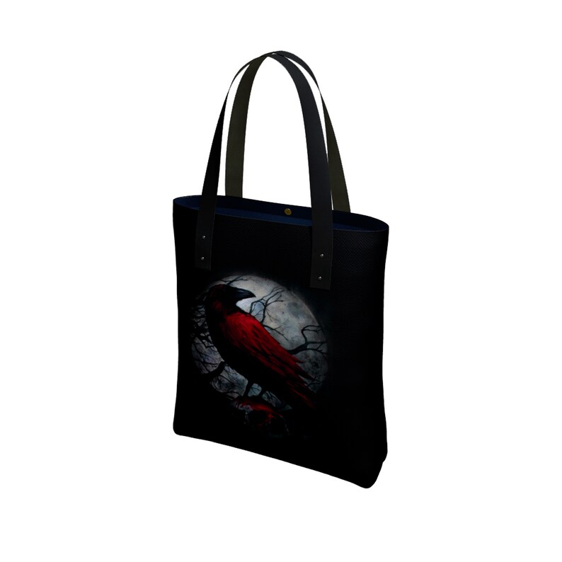 May include: Black tote bag with a red crow perched on a branch in front of a full moon. The crow is silhouetted against the moon.