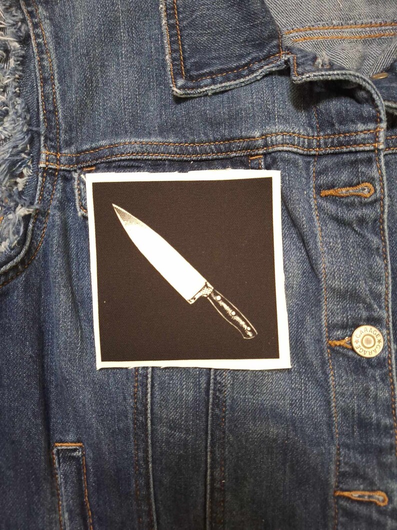 May include: A black and white iron-on patch with a white knife on a black background.