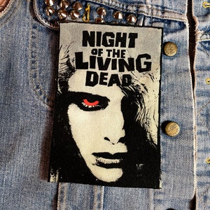 May include: A black and white patch with the text "Night of the Living Dead" and a close-up image of a zombie with red eyes.